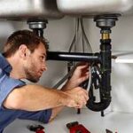 Un plombier-chauffagiste professionnel d'Argenteuil, outils en main, en train d'inspecter soigneusement une installation moderne de plomberie, avec en arrière-plan une malette d'outillage et des conduits en cuivre.