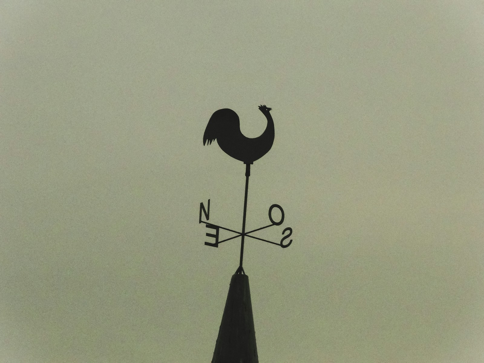 A silhouette of a rooster weather vane on a spire.