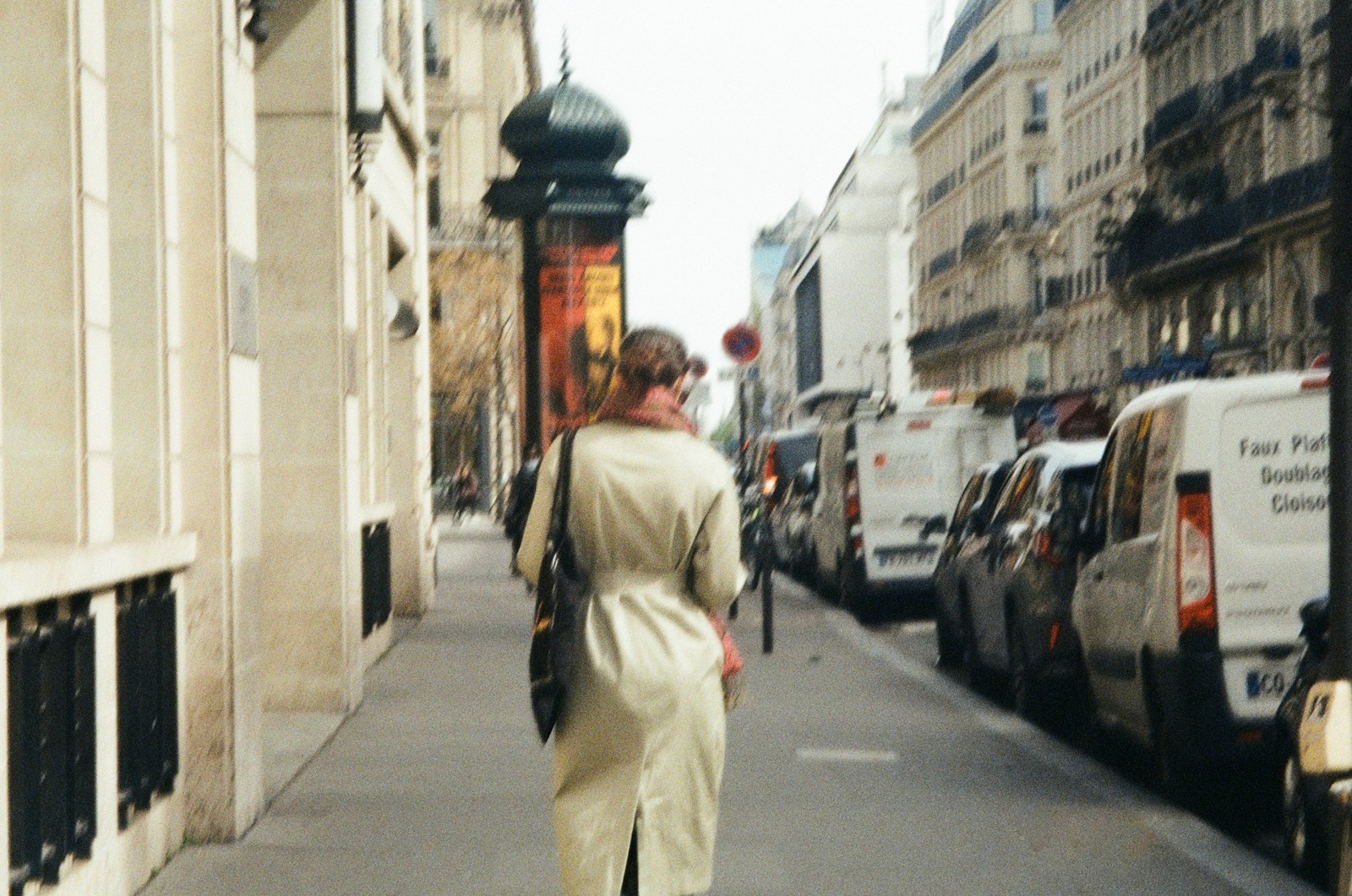 a woman walking down a street next to parked cars